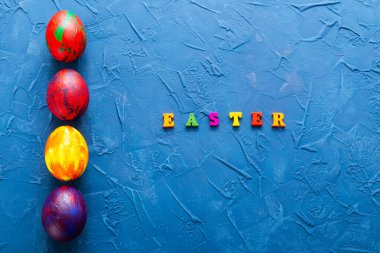 Çok renkli ahşap harfler mavi arka planda mutlu paskalya ve dekoratif renkli yumurta kelimelerini oluşturuyor. Üst görünüm.