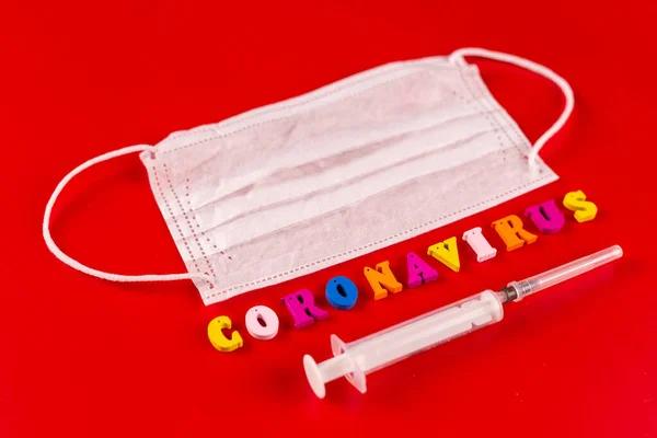 Słowo koronawirus wykonane z kolorowych liter na czerwonym tle. Napis na koronawirusie medycznej maski ochronnej. — Zdjęcie stockowe