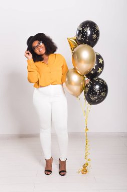 Tatiller, parti ve eğlence konsepti - Beyaz arka planda balonlarla şık görünen gülümseyen Afro-Amerikalı genç bir kadının portresi.