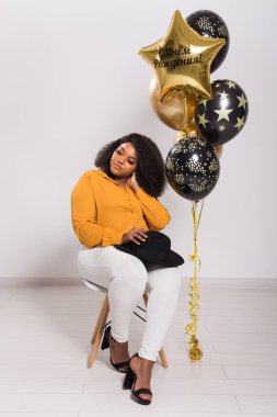 Tatiller, parti ve eğlence konsepti - Beyaz arka planda balonlarla şık görünen gülümseyen Afro-Amerikalı genç bir kadının portresi.