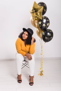 Tatiller, parti ve eğlence konsepti - Beyaz arka planda balonlarla şık görünen gülümseyen Afro-Amerikalı genç bir kadının portresi.
