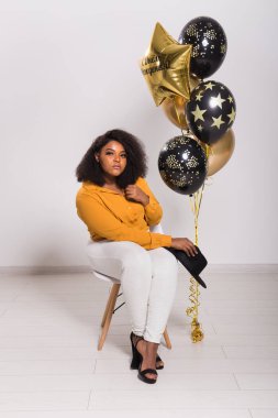 Tatiller, parti ve eğlence konsepti - Beyaz arka planda balonlarla şık görünen gülümseyen Afro-Amerikalı genç bir kadının portresi.