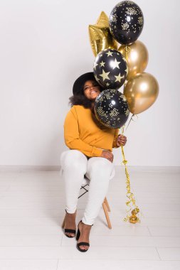 Tatiller, parti ve eğlence konsepti - Beyaz arka planda balonlarla şık görünen gülümseyen Afro-Amerikalı genç bir kadının portresi.