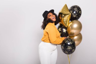 Tatiller, parti ve eğlence konsepti - Beyaz arka planda balonlarla şık görünen gülümseyen Afro-Amerikalı genç bir kadının portresi.