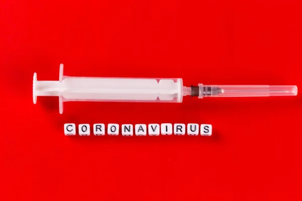 Concepto de pandemia y virus: texto del coronavirus con jeringa sobre fondo rojo. Nuevo coronavirus Covid-19 . —  Fotos de Stock