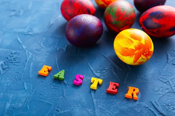 Mnohobarevná dřevěná písmena tvořící slova veselé velikonoce a dekorativní barevná vejce na modrém pozadí. — Stock fotografie
