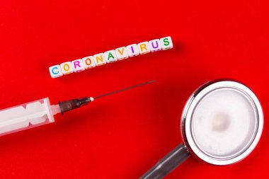 Pandemik ve virüs konsepti - Coronavirus metni ve kırmızı arka planda şırınga ve fonendoskop. Roman Coronavirus Covid-19.