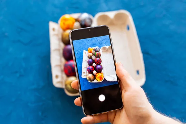 Holidays, tradition, technology and people concept - close up of man hands with smartphone taking picture of colored easter eggs.