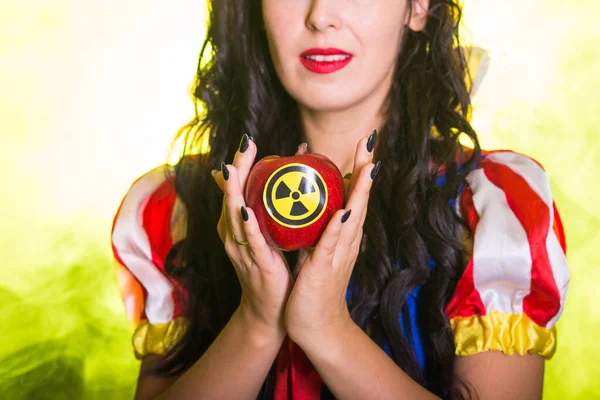 Woman dressed as Snow White holds Radioactive atomic nuclear ionizing radiation danger warning symbol on apple. Nuclear and radiation measurement concept. — Stock Photo, Image