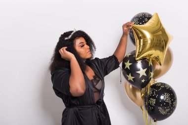 Tatiller, parti ve eğlence konsepti - Beyaz arka planda balonlarla şık görünen gülümseyen Afro-Amerikalı genç bir kadının portresi.