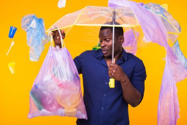 Çöp, plastik geri dönüşüm, kirlilik ve çevre kavramı sorunu - sarı arka planda çöp torbası taşıyan kafası karışmış adam