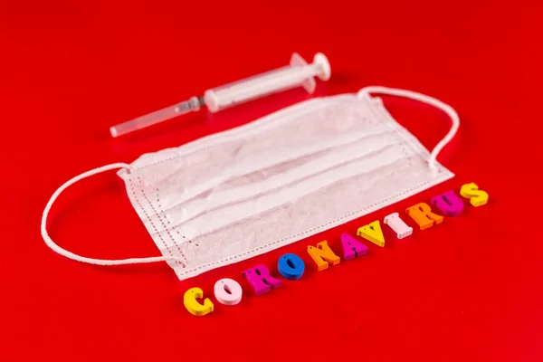 Słowo koronawirus wykonane z kolorowych liter na czerwonym tle. Napis na koronawirusie medycznej maski ochronnej. — Zdjęcie stockowe