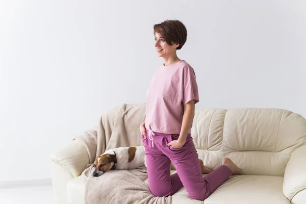 Mladá atraktivní žena oblečená v krásném barevném pyžamu pózující se psem jako modelka ve svém obývacím pokoji. Pohodlné spací oděvy, domácí relaxace a ženský módní koncept. — Stock fotografie