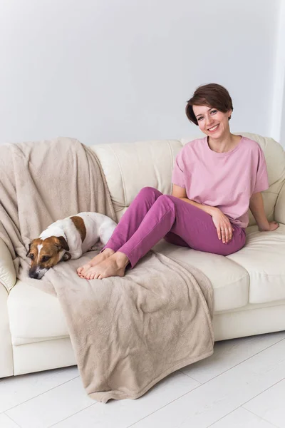 Jonge aantrekkelijke vrouw gekleed in prachtige kleurrijke pyjama poseren met hond als model in haar woonkamer. Comfortabele slaapkledij, huisontspanning en vrouwelijk modeconcept. — Stockfoto