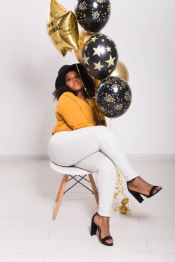 Tatiller, parti ve eğlence konsepti - Beyaz arka planda balonlarla şık görünen gülümseyen Afro-Amerikan genç kadının portresi.