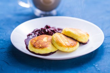 Breakfast and delicious concept - Pancakes from cottage cheese with jam, blue background. Sprinkle with icing sugar.