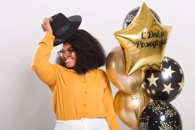 Tatiller, doğum günü partisi ve eğlenceli konsept - Beyaz arka planda balonlarla şık görünen gülümseyen Afro-Amerikan genç kadın portresi.