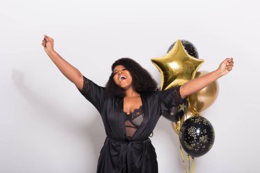 Tatiller, doğum günü partisi ve eğlenceli konsept - Beyaz arka planda balonlarla şık görünen gülümseyen Afro-Amerikan genç kadın portresi.