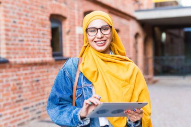 Arap kadın öğrenci. Sarı tesettürlü güzel Müslüman kız öğrenci elinde tablet tutuyor..