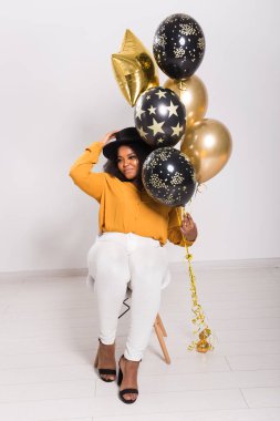 Tatiller, doğum günü partisi ve eğlenceli konsept - Beyaz arka planda balonlarla şık görünen gülümseyen Afro-Amerikan genç kadın portresi.