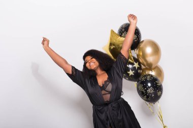 Tatiller, doğum günü partisi ve eğlenceli konsept - Beyaz arka planda balonlarla şık görünen gülümseyen Afro-Amerikan genç kadın portresi.