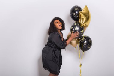 Tatiller, doğum günü partisi ve eğlenceli konsept - Beyaz arka planda balonlarla şık görünen gülümseyen Afro-Amerikan genç kadın portresi.