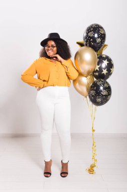 Tatiller, parti ve eğlence konsepti - Beyaz arka planda balonlarla şık görünen gülümseyen Afro-Amerikalı genç bir kadının portresi.