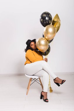 Tatiller, parti ve eğlence konsepti - Beyaz arka planda balonlarla şık görünen gülümseyen Afro-Amerikalı genç bir kadının portresi.