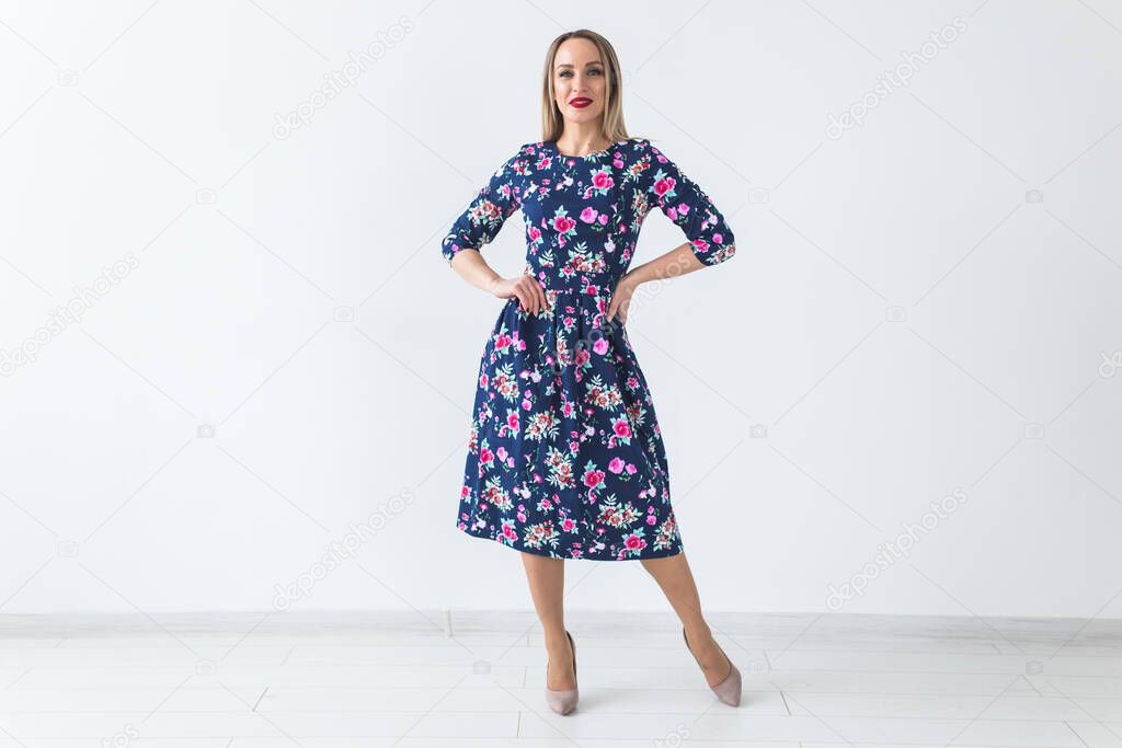 Fashionable young blonde woman in beautiful summer dress posing at white studio with copy space.