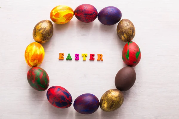 Multi-colored wooden letters making up the words happy easter and decorative colourful eggs on a white background with copy space.