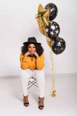 Tatiller, doğum günü partisi ve eğlenceli konsept - Beyaz arka planda balonlarla şık görünen gülümseyen Afro-Amerikan genç kadın portresi.