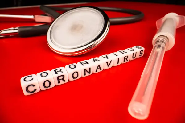 Concepto de pandemia y virus: texto del coronavirus con jeringa y fonendoscopio sobre fondo rojo. Nuevo coronavirus Covid-19 . —  Fotos de Stock