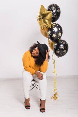 Tatiller, doğum günü partisi ve eğlenceli konsept - Beyaz arka planda balonlarla şık görünen gülümseyen Afro-Amerikan genç kadın portresi.