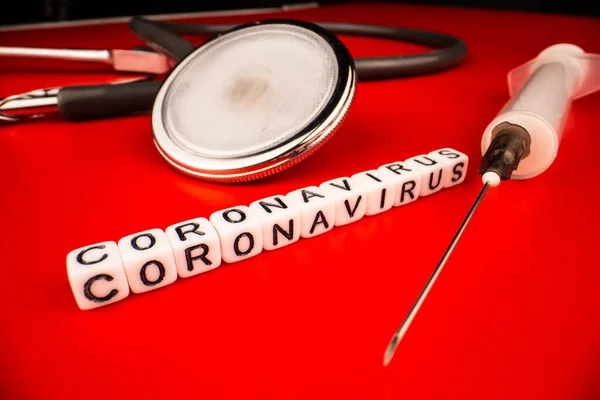 Concepto de pandemia y virus: texto del coronavirus con jeringa y fonendoscopio sobre fondo rojo. Nuevo coronavirus Covid-19 . —  Fotos de Stock