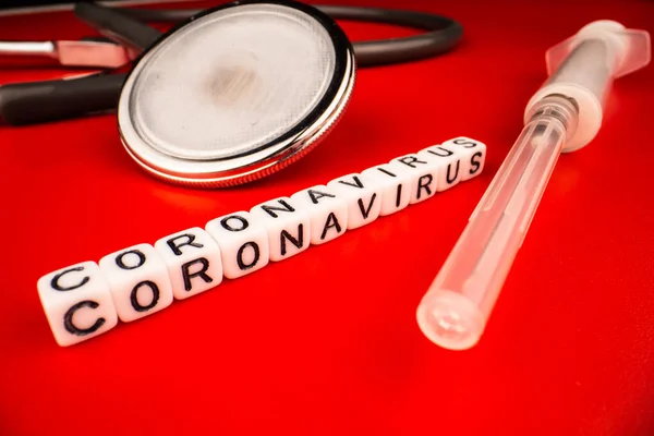 Koncepcja pandemii i wirusa - tekst koronawirusa ze strzykawką i fonendoskopem na czerwonym tle. Nowy koronawirus Covid-19. — Zdjęcie stockowe