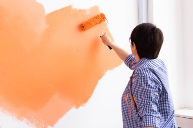 Yenileme, dekorasyon ve onarım konsepti - orta yaşlı kadın yeni evinde duvar boyuyor.