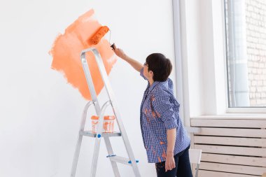 Yenileme, dekorasyon ve onarım konsepti - orta yaşlı kadın yeni evinde duvar boyuyor.