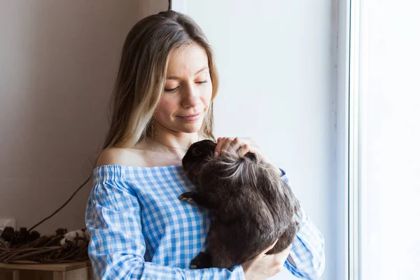 Mascotas y concepto de Pascua - Chica atractiva abrazando conejo marrón en casa . — Foto de Stock