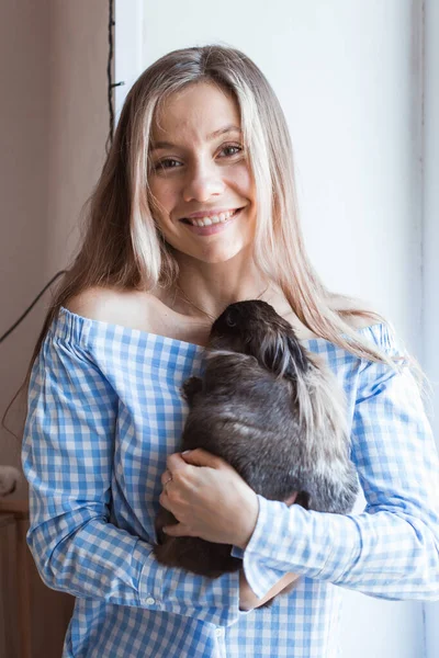 Pet e conceito de Páscoa - Menina atraente abraçando coelho marrom em casa . — Fotografia de Stock