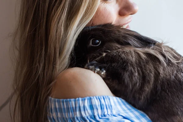 Mascotas y concepto de Pascua - Muchacha atractiva abrazando conejo marrón en casa, primer plano . — Foto de Stock