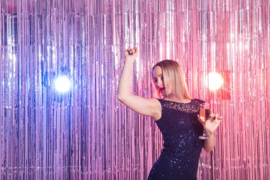 Parti, içkiler, tatiller ve kutlama konsepti. Parlak arka planda bir bardak köpüklü şarapla gülen kadın..