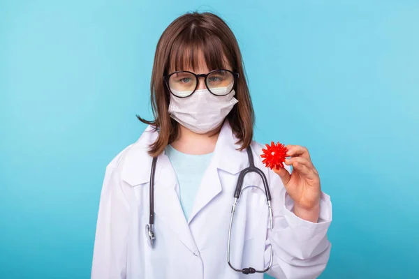 Концепция вируса, пандемии, карантина и вспышки - ребенок в костюме врача держит модель коронавируса COVID-19 на синем фоне . — стоковое фото