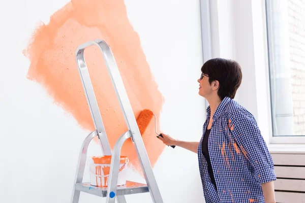 Concetto di ristrutturazione, ridecorazione e riparazione - parete di pittura donna di mezza età in una nuova casa. — Foto Stock