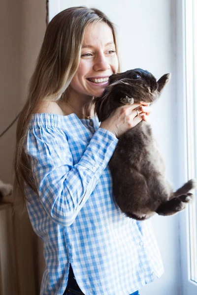 Huisdier en Pasen concept - Gelukkig meisje knuffelen bruin konijn thuis. — Stockfoto