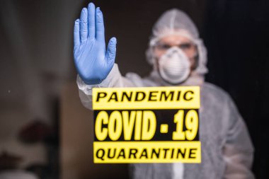 Koruyucu giysili ve koruyucu tıbbi maskeli bir adam dur işareti gösteriyor. Epidemiyoloji uzmanı palmiyeyi durdurdu. Coronavirüs veya covid-19 ve salgını durdurun. Evde kal. Karantina konsepti.