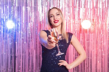 Parti, içkiler, tatiller ve kutlama konsepti. Parlak arka planda bir bardak köpüklü şarapla gülen kadın..