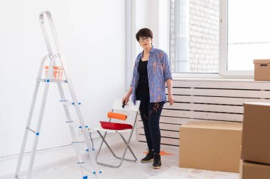 Yenileme, dekorasyon ve onarım konsepti - orta yaşlı kadın yeni evinde duvar boyuyor.