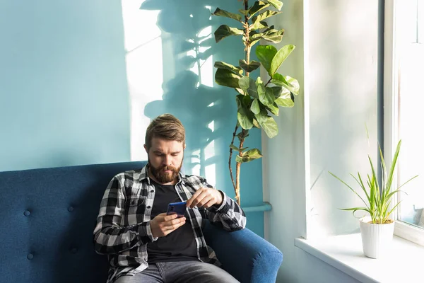 Технологии и концепция досуга - Красивый человек, использующий смартфон дома . — стоковое фото