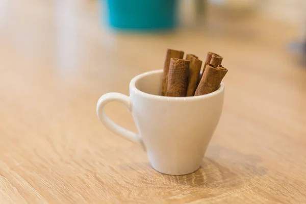 Beker met aromatische kaneelstokjes op houten tafel, close-up. — Stockfoto