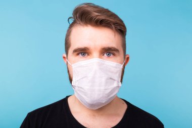 Siyah tişörtlü yakışıklı genç adam izole edilmiş mavi arka planda tıbbi maske takıyor, yakın plan. Covid-19, koronavirüs ve virüs konsepti.